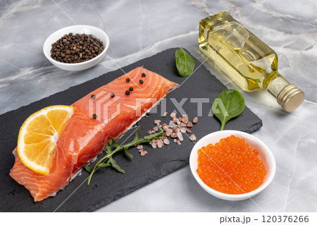 Fillet of raw salmon fish with arugula, basil and lemon on the cutting board with red caviar. Fillet of raw salmon fish with arugula, basil and lemon on the cutting board with red caviar. 120376266