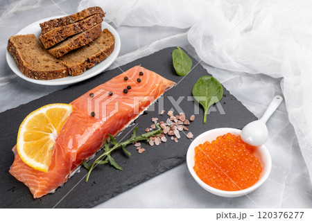 Fillet of raw salmon fish with arugula, basil and lemon on the cutting board with red caviar. Fillet of raw salmon fish with arugula, basil and lemon on the cutting board with red caviar. 120376277