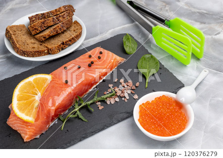 Fillet of raw salmon fish with arugula, basil and lemon on the cutting board with red caviar. Fillet of raw salmon fish with arugula, basil and lemon on the cutting board with red caviar. 120376279