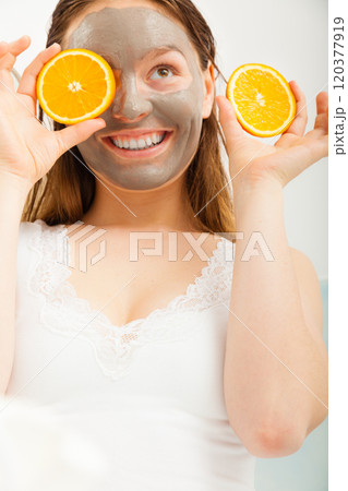 Woman with mud facial mask holds orange slice 120377919