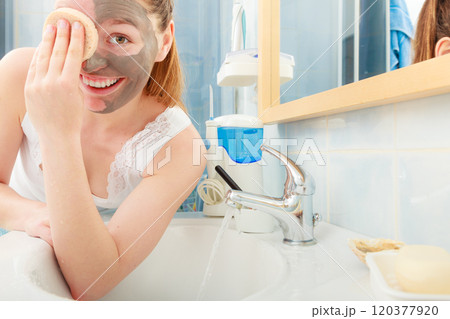woman removing facial clay mud mask in bathroom 120377920