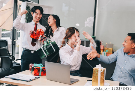 full length view of a group of business team wearing red Santa hat and exchange gift box together in the office for Christmas. full length view of a group of business team wearing red Santa hat and exchange gift box together in the office for Christmas. 120378459