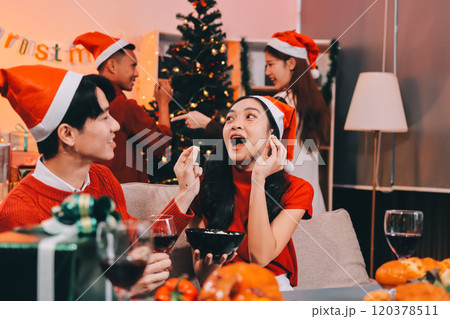 Group of young Asian man and women as friends having fun at a New Year's celebration, holding gift boxes standing by Christmas tree decoration, midnight countdown Party at home with holiday season. 120378511