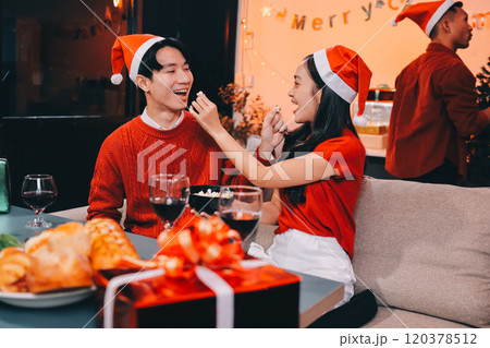 Group of young Asian man and women as friends having fun at a New Year's celebration, holding gift boxes standing by Christmas tree decoration, midnight countdown Party at home with holiday season. 120378512