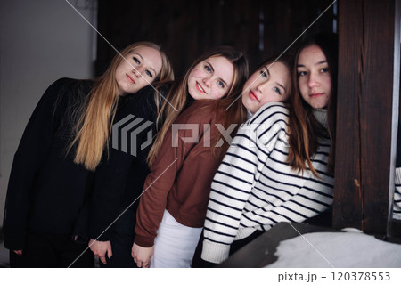 Group of four young women posing for a winter photoshoot, showcasing their friendship and leaning on each other 120378553