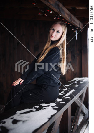 Young lady sitting on a snowy bench under a wooden shelter, savoring a tranquil winter day 120378560