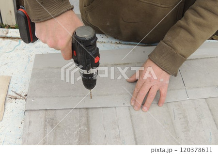 A construction worker fastens gray metal sheets together that are lying on a blue rusty table, using a screwdriver and self-tapping screws A construction worker fastens gray metal sheets together that are lying on a blue rusty table, using a screwdriver and self-tapping screws 120378611