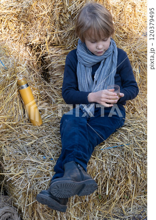 Little boy drinking tea sitting on bales of straw Little boy drinking tea sitting on bales of straw 120379495