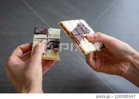 Piece of trend Dubai white chocolate with halva paste in woman hands. Confectionery handmade sweets at home in the kitchen.  120380347
