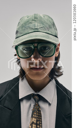 Close-up portrait of stylish young guy wearing green cap and oversized green sunglasses, black blazer, white shirt and pattern tie, posing against studio background Close-up portrait of stylish young guy wearing green cap and oversized green sunglasses, black blazer, white shirt and pattern tie, posing against studio background 120381660