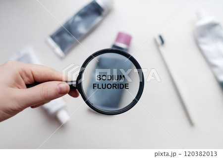 Sodium fluoride in natural toothpaste. Magnifying glass is directed at a tube with a list of ingredients of a safe product. Safe toothpaste composition Sodium fluoride in natural toothpaste. Magnifying glass is directed at a tube with a list of ingredients of a safe product. Safe toothpaste composition 120382013