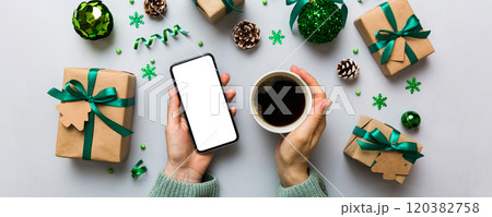 Above view of female hand holding smart phone with hot cup of coffee. Christmas decoration on colored background 120382758