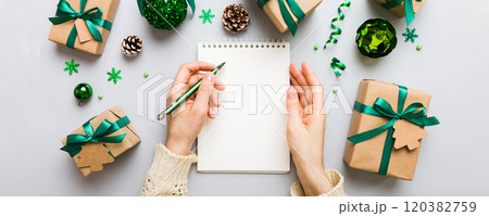 Woman writing Christmas to do list on notebook on colored background with xmas decorations Woman writing Christmas to do list on notebook on colored background with xmas decorations 120382759