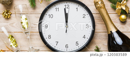New year celebration concept with a bottle of champagne and two glasses toasting. Christmas gift box, alarm clock and fir tree branch on colored table. Top view Copy space New year celebration concept with a bottle of champagne and two glasses toasting. Christmas gift box, alarm clock and fir tree branch on colored table. Top view Copy space 120383589