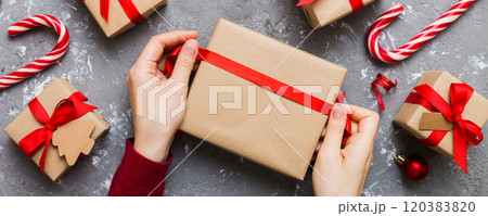 Woman is packing surprise gift for Christmas holidays, sitting at workplace with craft tools, top view. Woman wrapping Christmas gift at colored table 120383820