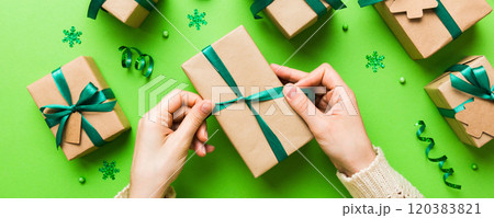 Woman is packing surprise gift for Christmas holidays, sitting at workplace with craft tools, top view. Woman wrapping Christmas gift at colored table 120383821
