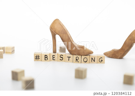 A beautiful high-heeled wooden shoe stand on wooden cubes with the inscription BE STRONG against white background A beautiful high-heeled wooden shoe stand on wooden cubes with the inscription BE STRONG against white background 120384112