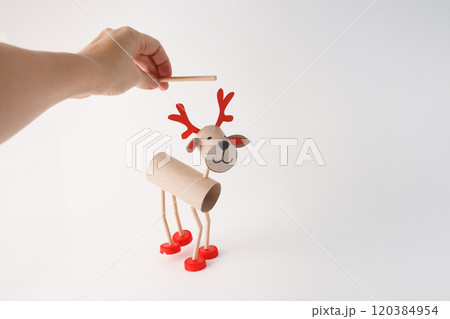 Hand holding DIY reindeer puppet made from cardboard tubes, plastic caps, and paper details. Christmas craft and holiday decoration concept, easy activity to do, paper roll craft for kid, 120384954