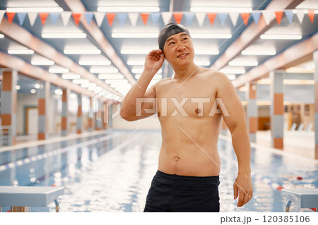 Man wearing special hat for swimming. Asian man standing in indoor swimming pool. Professionale male swimmer is going to swim. Man wearing special hat for swimming. Asian man standing in indoor swimming pool. Professionale male swimmer is going to swim. 120385106