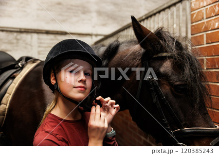 Young little teenager kid girl wearing protective helmet before riding horse stable ranch. Horse ride school farm life. Cute little blond girl kid use protection equipment apparel. Equine hobby work Young little teenager kid girl wearing protective helmet before riding horse stable ranch. Horse ride school farm life. Cute little blond girl kid use protection equipment apparel. Equine hobby work 120385243
