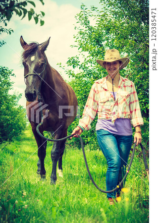 Western woman walking on green meadow with horse Western woman walking on green meadow with horse 120385471