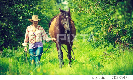 Western woman walking on green meadow with horse 120385472
