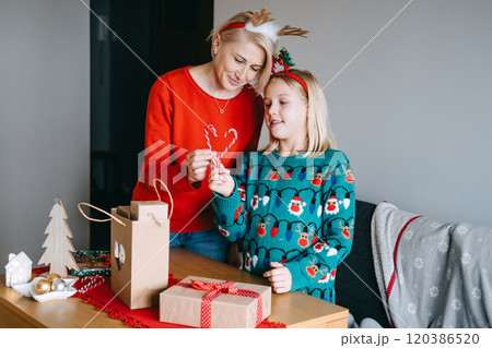 Mother and daughter sharing simple Christmas pleasures while decorating gifts. Holiday comfort, festive moments, togetherness, Christmas joy, creating memories. 120386520