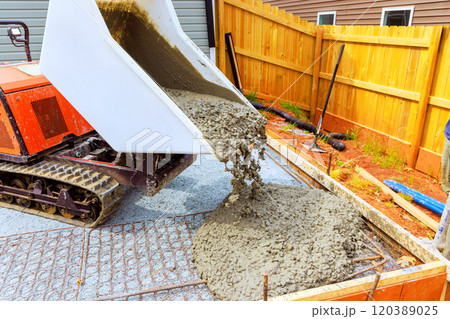 Concrete mixer discharges fresh concrete into prepared foundation area construction site is marked by wooden frames gravel on using compact tracked dumper 120389025