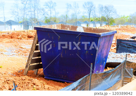 Dumpster is positioned at construction site surrounded by dirt mounds new homes under construction being built 120389042