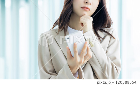スマホを持って悩む女性・ビジネスウーマン 120389354