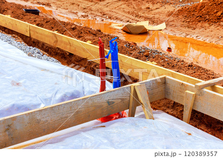 Construction site place wooden frames into freshly dug ground, while plastic boundaries area is preparation foundation 120389357