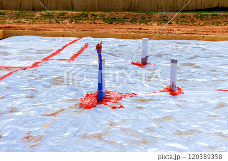 Workers prepare for foundation work by laying plastic sheeting pipes at construction site 120389358