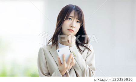 スマホを持って悩む女性・ビジネスウーマン 120389910