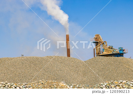 white steam rising up from pipe of small asphalt factory at day time with piles of gravel in a foreground white steam rising up from pipe of small asphalt factory at day time with piles of gravel in a foreground 120390213