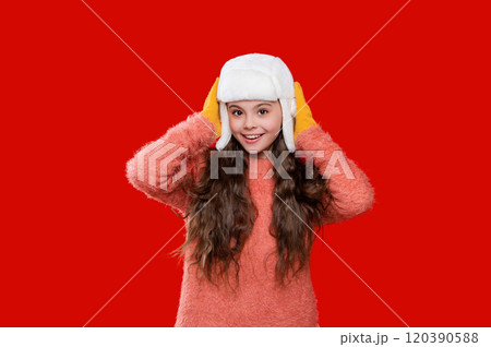 Teen kid girl wearing warm knitted winter earflap hat and sweater isolated on red 120390588