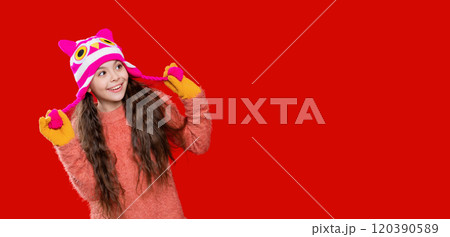 Teenager knitted fashion. Outdoor lifestyle fashion. Teenager girl in a winter warm hat isolated on red. Happy girl in winter hat. Winter fashion style. Innocent joy 120390589