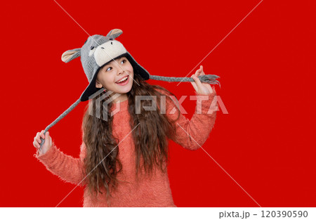 Outdoor lifestyle fashion. Teenager girl in a winter warm hat isolated on red. Happy girl in winter hat. Winter fashion style. Teenager knitted fashion. Childhood innocence 120390590