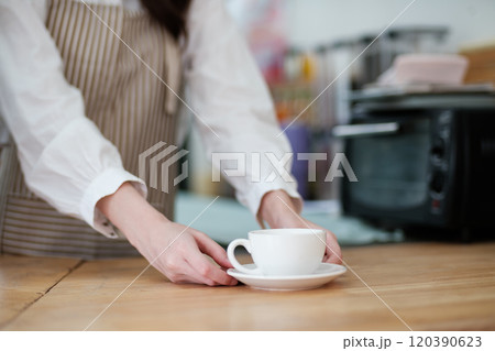 Barista placing a freshly brewed coffee cup on a wooden counter in a cozy cafe. 120390623