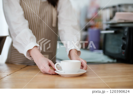 Barista placing a freshly brewed coffee cup on a wooden counter in a cozy cafe. 120390624
