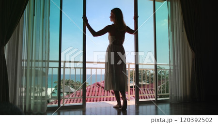 Tourist is entering the terrace of her hotel room enjoying the warm summer breeze and the beautiful view from her balcony Tourist is entering the terrace of her hotel room enjoying the warm summer breeze and the beautiful view from her balcony 120392502