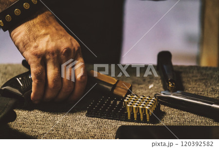 Man handling ammunition. There is a hand holding a handgun magazine, with a tray of bullets and parts of a firearm visible on a surface.  120392582