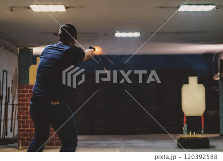 Person firing a handgun at an indoor shooting range with humanoid target and visible muzzle flash. Aim and fire, Training. Firearm 120392588