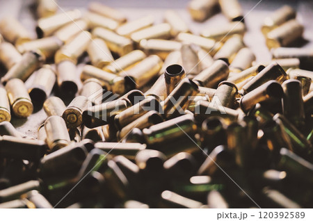The image shows a pile of spent bullet casings. They appear to be brass-colored and are used cartridges from firearms. 120392589