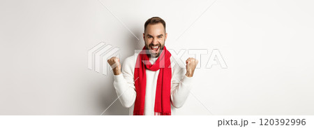 Christmas holidays and New Year concept. Happy man celebrating victory, winning and making fist pumps, achieve goal, saying yes while standing over white background 120392996