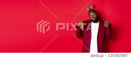 Merry Christmas. Silly and funny Black man in party headband, imitating bunny or cute puppy, standing over red background 120392997