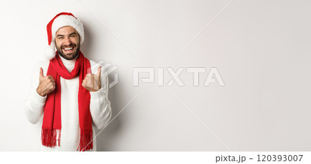 Christmas holidays. Happy man at good new year party showing thumb up, enjoying celebration, wearing santa hat and red scarf, white background 120393007