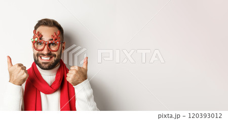 Christmas, New Year and celebration concept. Happy and satisfied man with beard, wearing party glasses, showing thumbs up in approval or like, standing over white background 120393012