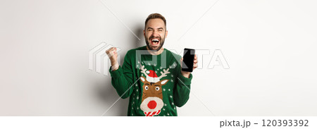 Christmas holidays and shopping concept. Excited bearded man showing mobile screen and rejoicing, winning in internet, standing over white background 120393392
