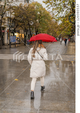 Woman wearing a white coat walking on a rainy street with red umbrella Woman wearing a white coat walking on a rainy street with red umbrella 120393537