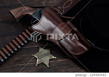 Marshal star badge with gun, holster and gun belt with old west hat on table. Top view. Marshal star badge with gun, holster and gun belt with old west hat on table. Top view. 120393581